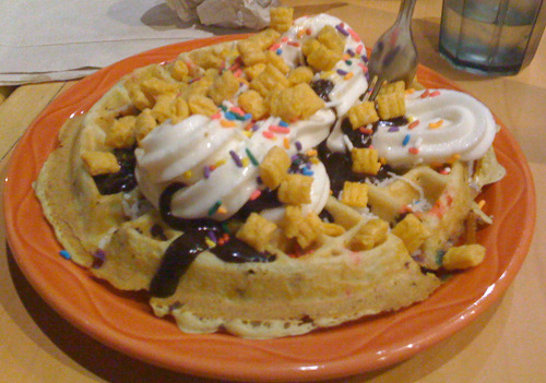 Circus Waffle
A brownie and muliticolored sprinkle infused waffle topped with vanilla soft serve, coconut shavings, banana, hot fudge, Cap&#8217;n Crunch, and sprinkles.
(submitted by Frank M)